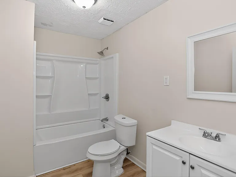 Full bathroom with tub/shower combo, built-in surround shelving, and a vanity with mirror and storage below.