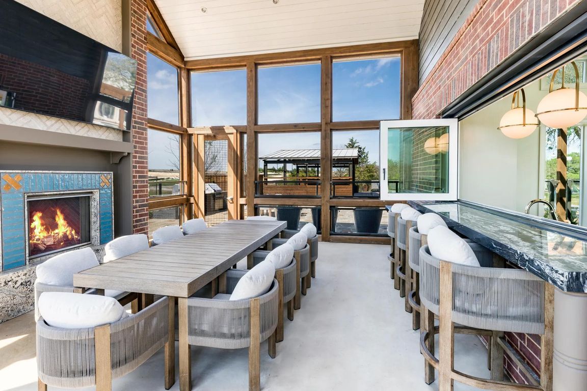 Screened-in porch with a harvest dining table, an adjacent catering kitchen and entertainment lounge inside, plus a cozy outdoor fireplace.