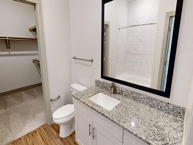 Apartment Bathroom with large wall mirror and Wood Style Flooring.