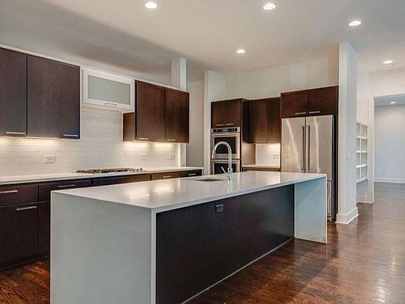 Open design kitchen with fridge, 2-ovens cooktop, microwave, long island with a deep kitchen sink. Dark wood cabinetry and white countertops.