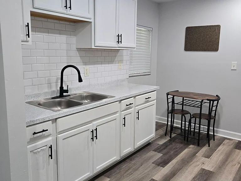 Updated kitchen with ample white cabinetry, double-basin sink, tile backsplash, and a small dining nook by the window.