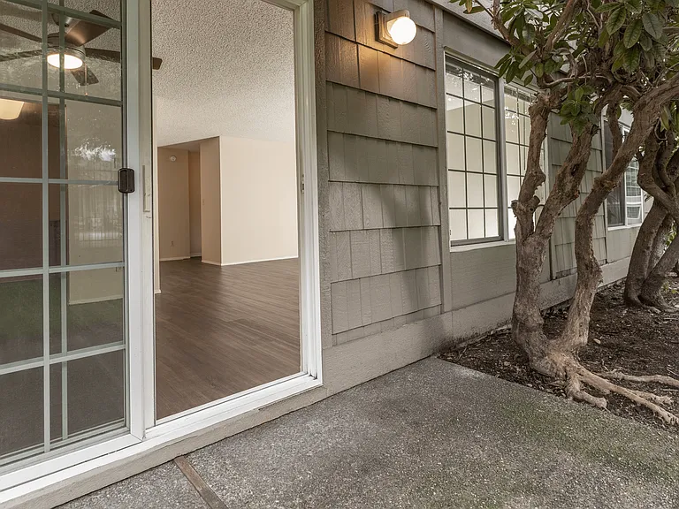 Inviting patio entrance with sliding glass doors opening to a spacious living room with wood flooring and large windows. Inviting patio entrance with sliding glass doors opening to a spacious living room with wood flooring and large windows.