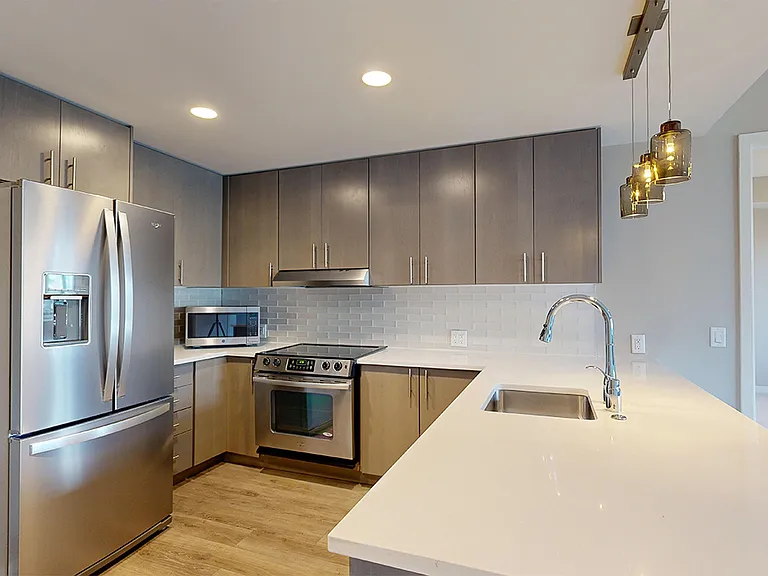 Apartment kitchen with stainless steel appliances, quartz countertops and wood-style flooring.