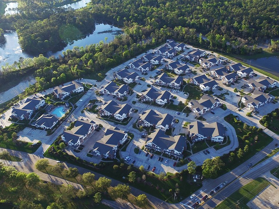 Aerial view of a serene apartment community surrounded by lush greenery and sparkling water features, showcasing modern villas with immaculate landscaping.
