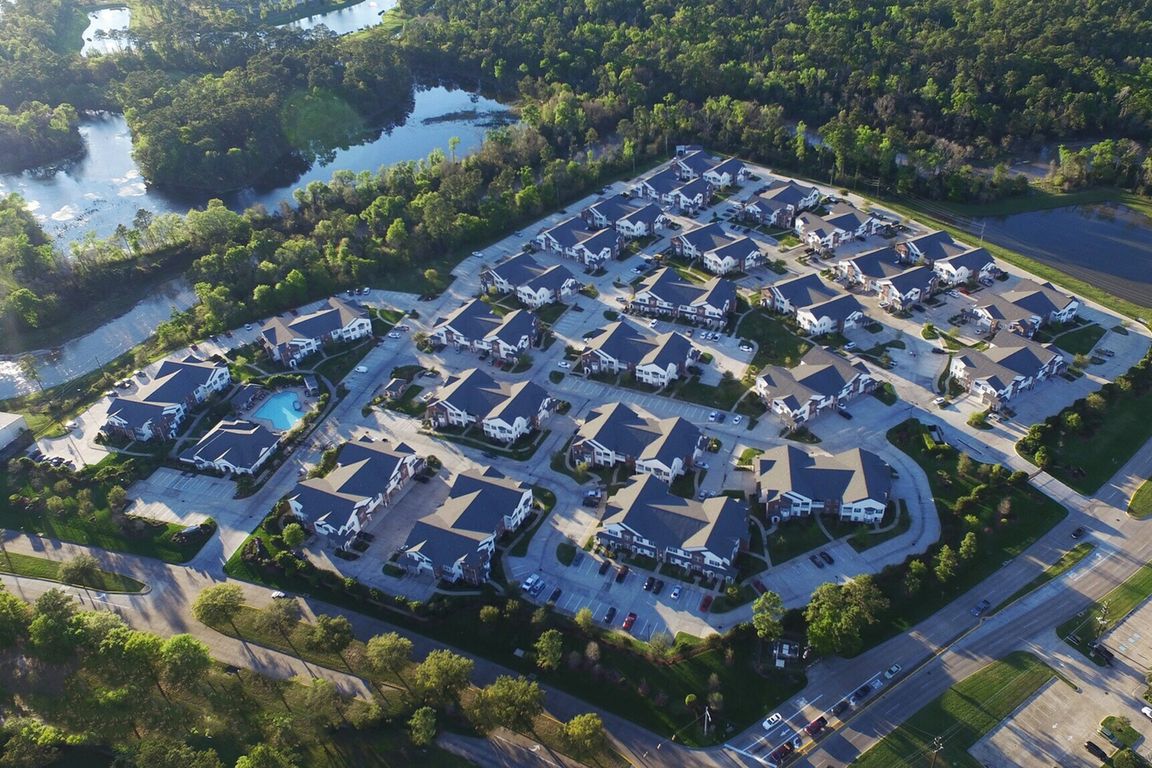 Aerial view of a serene apartment community surrounded by lush greenery and sparkling water features, showcasing modern villas with immaculate landscaping.