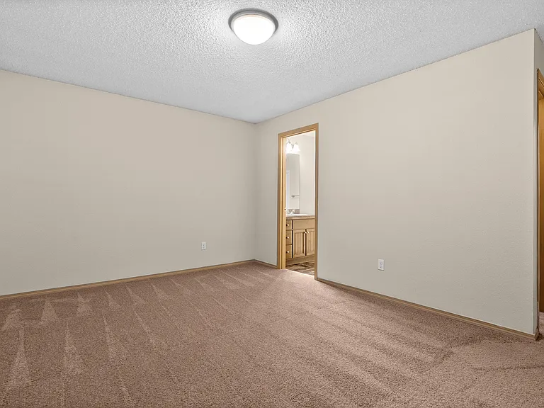 Spacious bedroom with soft carpet flooring, neutral walls, and an adjoining bathroom with a modern vanity. Spacious bedroom with soft carpet flooring, neutral walls, and an adjoining bathroom with a modern vanity.