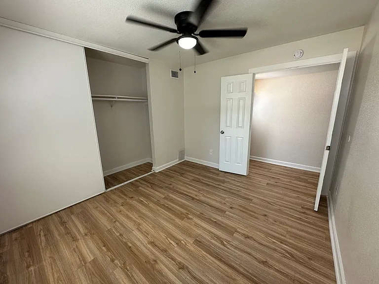 Modern bedroom with elegant wood-style flooring, open closet space, and contemporary ceiling fan. Modern bedroom with elegant wood-style flooring, open closet space, and contemporary ceiling fan.