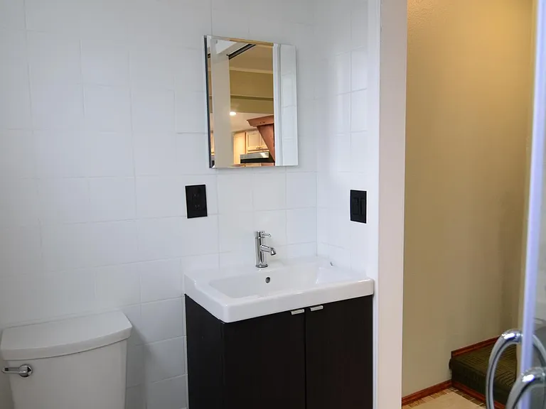 Bath with tile floor, tile walls, newer window, vanity, mirror and energy efficient toilet.