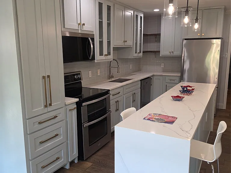 Modern kitchen featuring a waterfall-edge island with seating, light gray cabinetry, stainless steel appliances, and wood-finish flooring