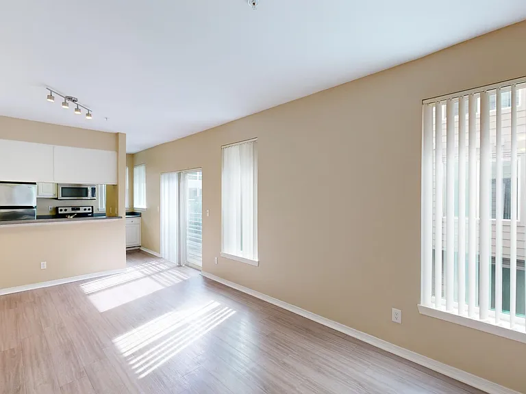 Apartment kitchen with stainless steel appliances, dining and living room with wood-style flooring.
