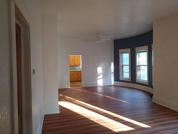 Living room, dining room with ceiling fan. Kitchen cupboards visible in background.