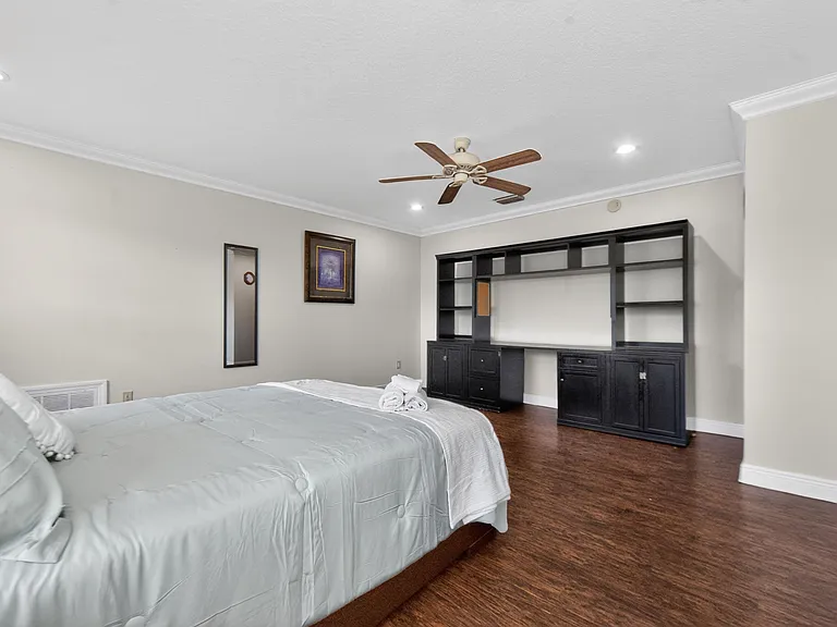 Spacious bedroom with hardwood floors, ceiling fan, recessed lighting, and built-in shelving with ample storage.