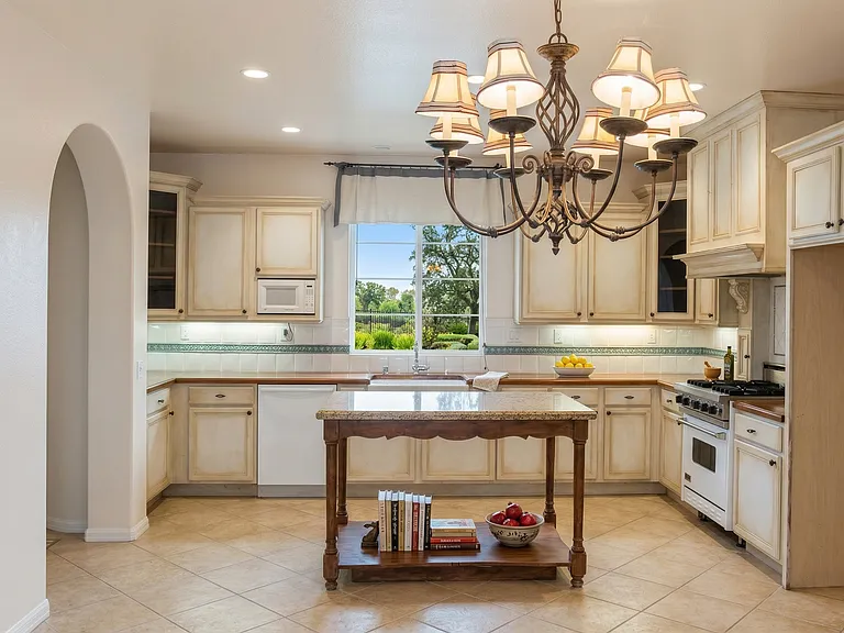 Beautifully designed French country kitchen featuring wood countertops, farmhouse sink, custom cabinetry, and elegant lighting