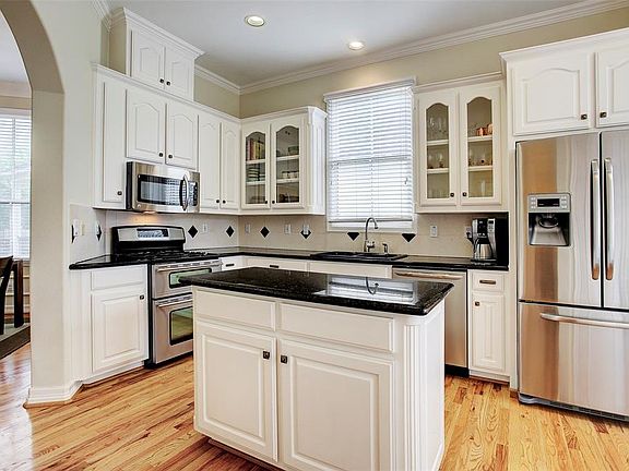Hardwood floors continue into the kitchen which has black granite counters, modern tile back splash, stainless appliances and two sets of glass-front 