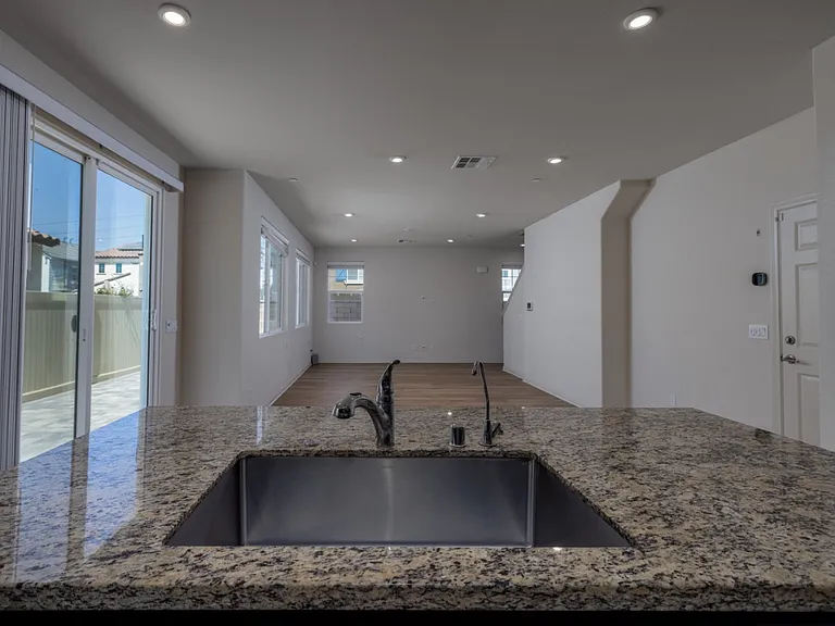 Modern open layout connecting the kitchen and living area, featuring recessed spot lighting, solar-powered efficiency, and large windows that fill the space with natural light for a bright and inviting atmosphere.