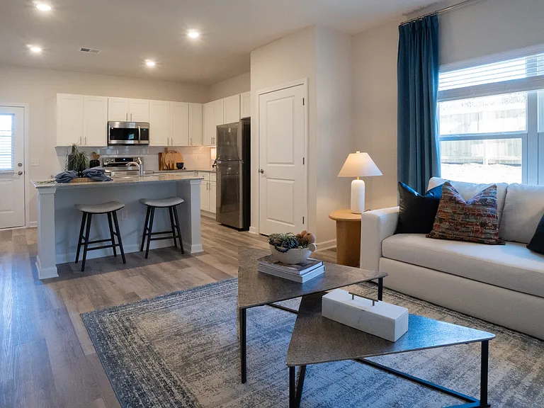 Living room with large windows that let in a ton of natural light. Looking into the kitchen and the back patio door.