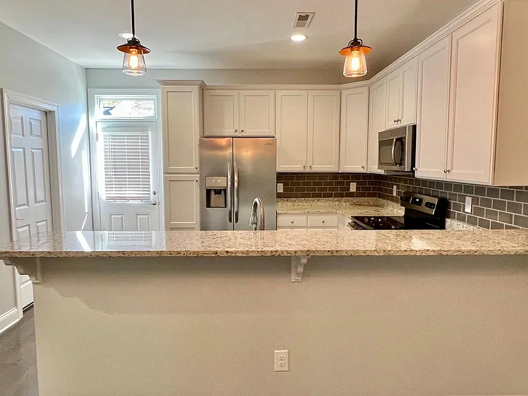 Spacious kitchen with modern white cabinets, granite counter tops, tile backsplash, stainless steel fridge, sink, oven/range, and microwave.