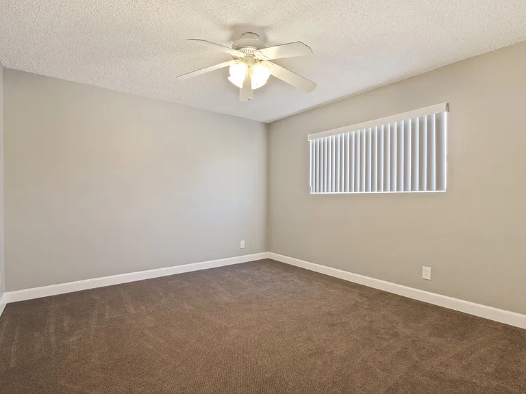 Bedroom with carpet floors, ceiling fan, vertical blinds on the window