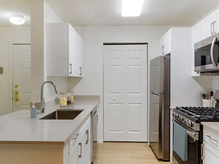 Renovated Package I bath with white cabinetry, beige quartz countertops, white tile backsplash, stainless steel appliances, and hard surface flooring