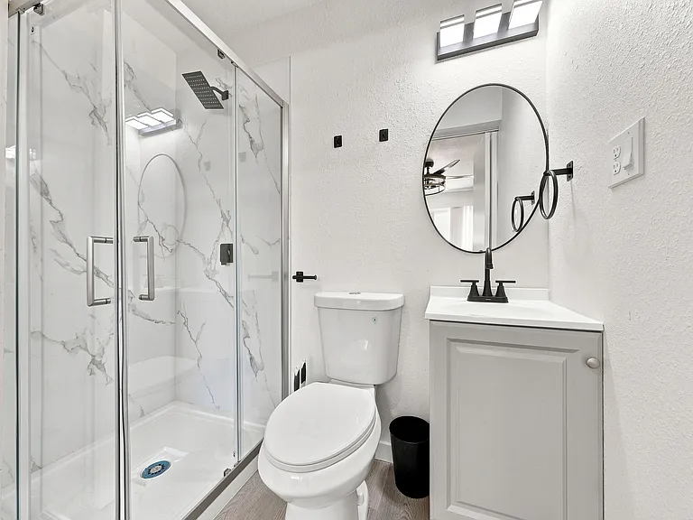 Updated bathroom with a glass-enclosed shower, sleek vanity with black fixtures, and easy-care flooring.