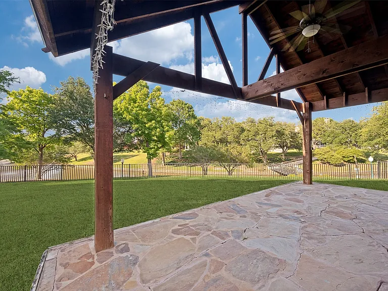 Expansive covered patio featuring flagstone flooring, exposed wood beams, and a ceiling fan