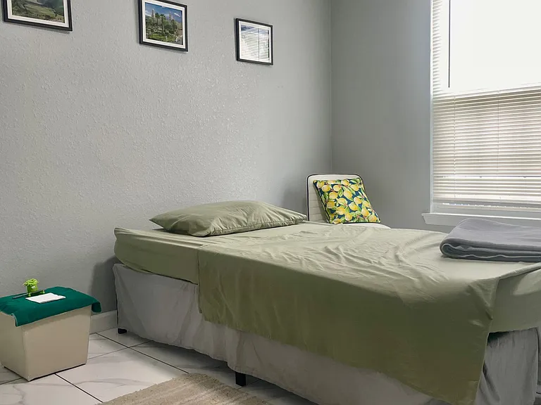 Furnished bedroom with a comfortable bed, tiled flooring, and a large window with blinds for natural light and privacy.