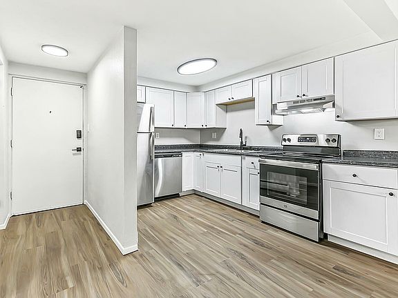 Bright and modern kitchen with sleek white cabinets, stainless steel appliances, and elegant wood flooring.