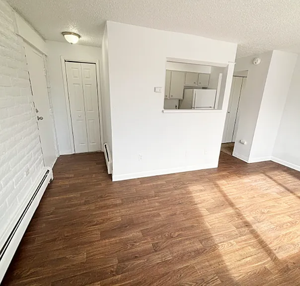 Bright open-plan living area with sleek wooden flooring, leading into a charming kitchen nook, perfect for modern living.