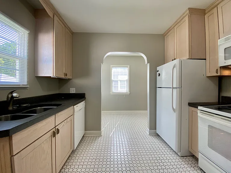 Bright and inviting kitchen featuring sleek black countertops, light wood cabinetry, and a stylish arched doorway leading to a sunlit dining area. Bright and inviting kitchen featuring sleek black countertops, light wood cabinetry, and a stylish arched do