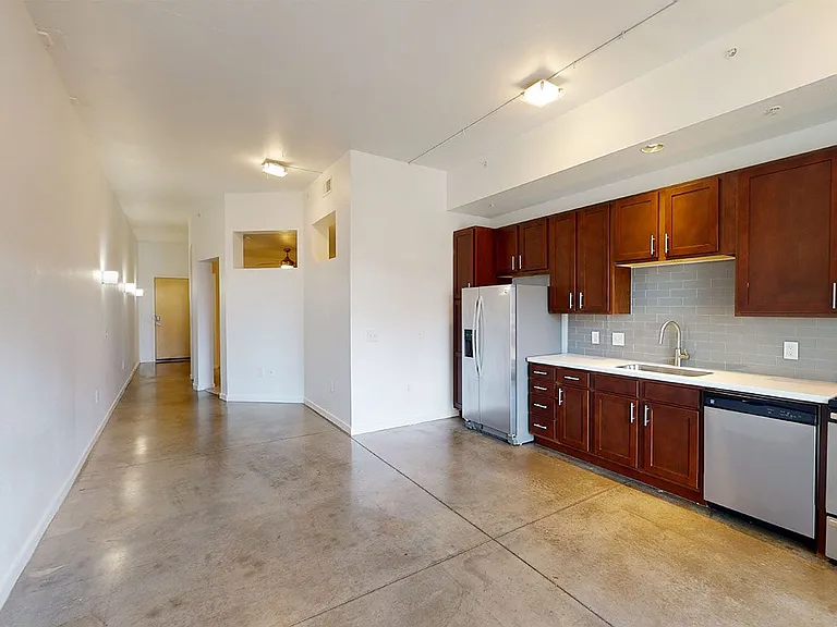 Apartment kitchen with stainless steel appliances, dining and living room with polished concrete flooring.