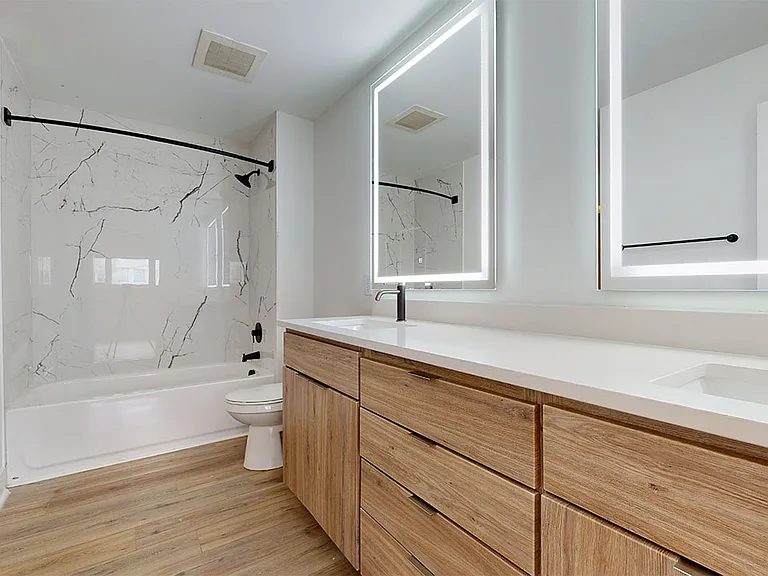 Apartment bathroom with wood-style flooring, double sinks and LED vanity mirror.