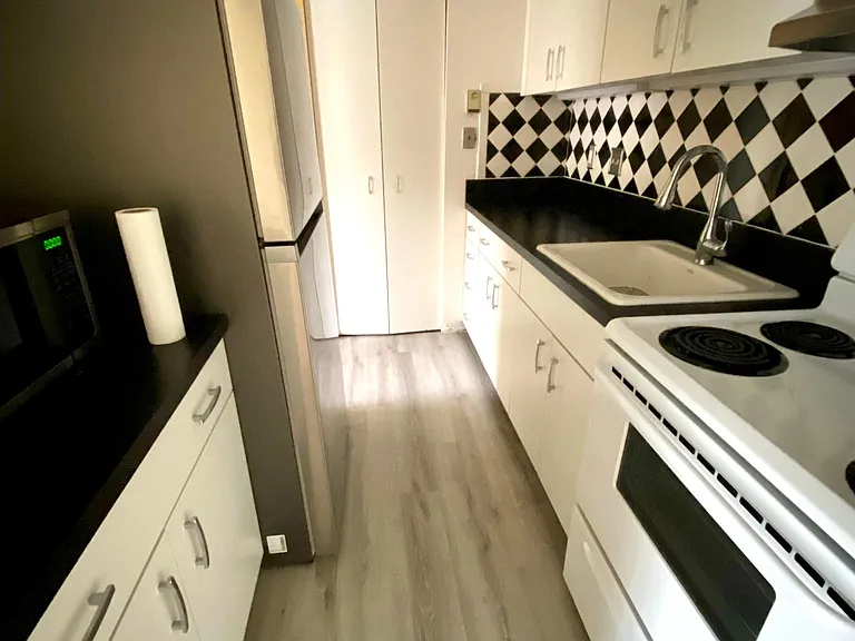 Classic 1950s-inspired, sleek, modern kitchen with stainless steel fridge and wide-plank wood flooring.
