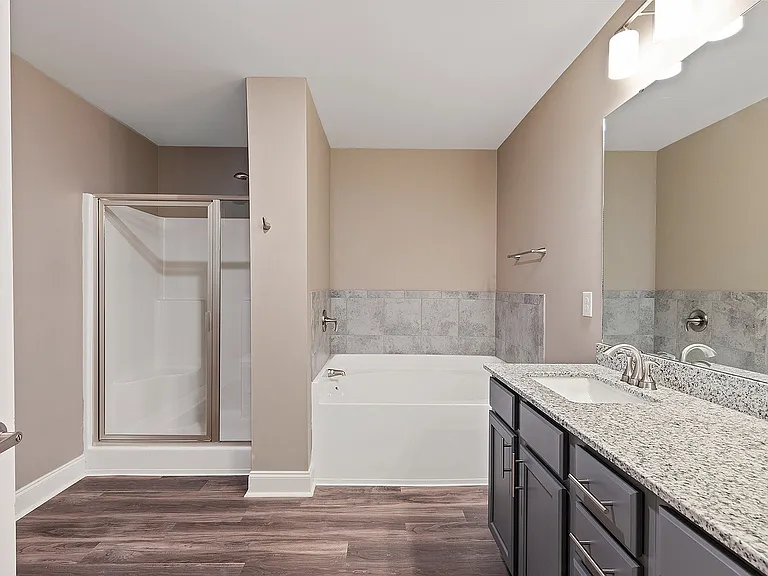 Modern bathroom featuring a granite countertop vanity, sleek glass shower, and relaxing bathtub.