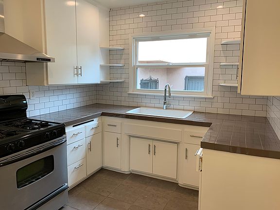 The kitchen has been redone with stylish subway tiles, a large honed granite sink with a goose neck faucet. Stainless oven with a statement stainless hood above. The kitchen has plenty of storage and counter space. Bright & cheerful with the large window,