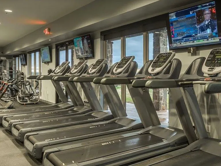 Dedicated fitness center featuring multiple treadmills, exercise bikes, weight machines, and large exterior windows