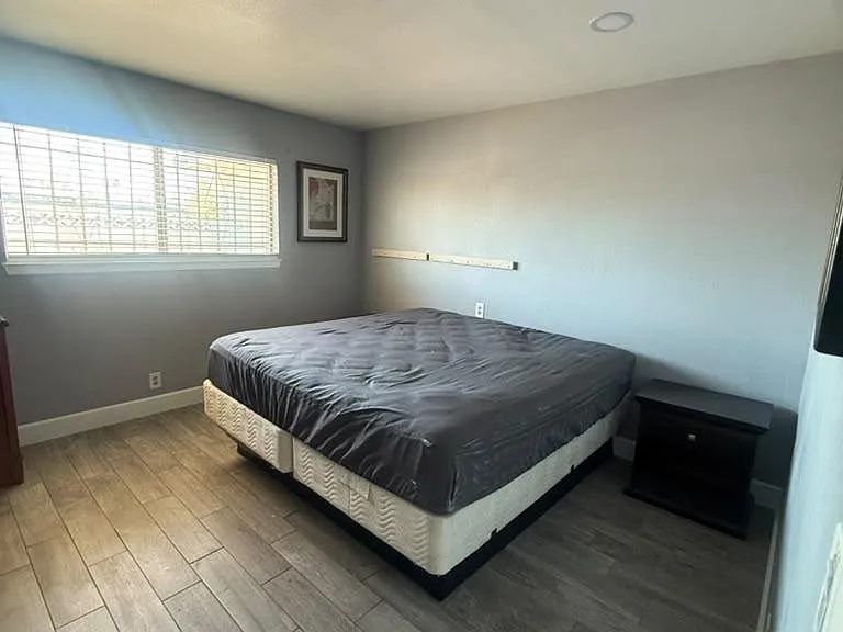 Spacious bedroom with a large window, wood-look tile flooring, and room for a full or queen bed plus side tables.