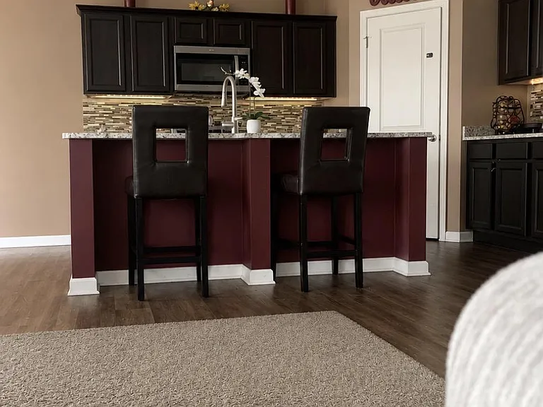 Kitchen features a large breakfast bar with seating, dark cabinetry, and a mosaic backsplash with built-in microwave.