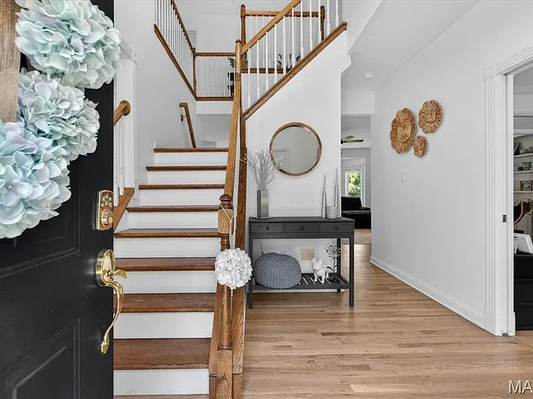 Open entryway with a dark paneled door featuring brass hardware, wood-finish flooring, a wood staircase with white risers and spindles, and a recessed doorway