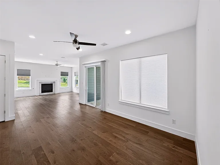 Spacious room featuring wood-finish flooring, a fireplace with a white mantel, multiple windows, recessed lighting, and a glass sliding door