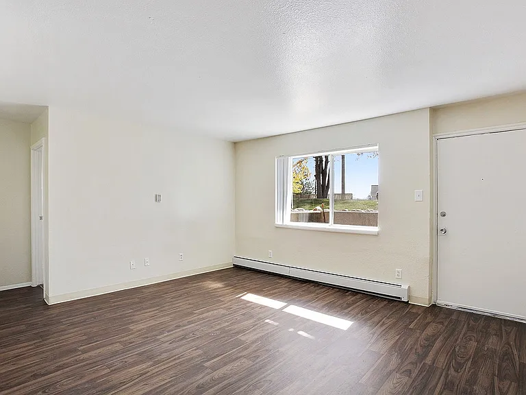 Bright living room with elegant wood flooring, large window, and modern neutral walls, inviting natural light and providing a spacious ambiance.