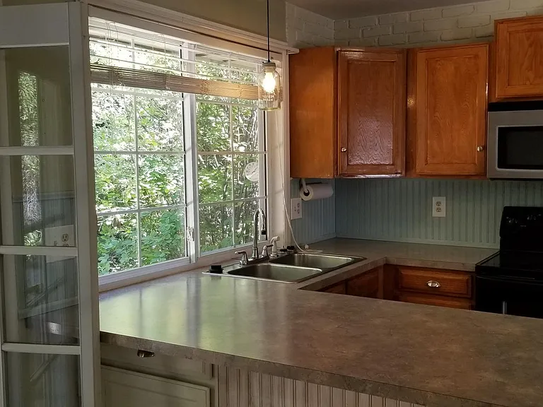 Bright kitchen with lots of windows that looks out over greenery in back yard.