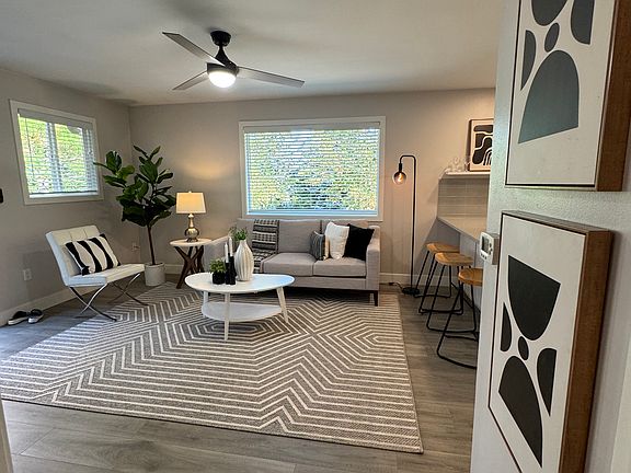 Bright open living room with large picture window, ceiling fan, and durable plank flooring.