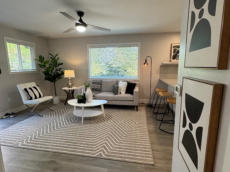 Bright open living room with large picture window, ceiling fan, and durable plank flooring.
