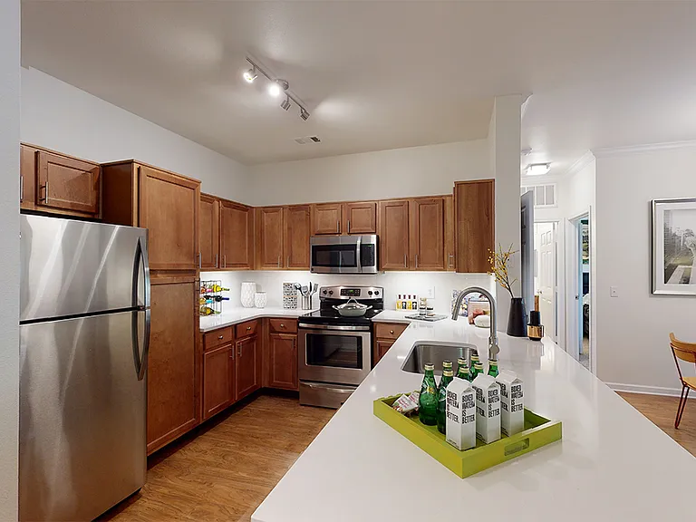 Apartment kitchen with stainless steel appliances and wood-style flooring. Quartz-style countertops (shown here) are available in select homes.