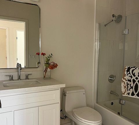 Beautiful bathroom with white shaker cabinet, white quartz counter top, chrome fixtures and accessories, tub/shower with tile surround and accent niche, glass door, tile floors, toto toilet