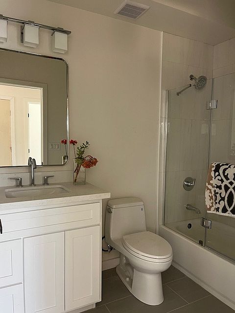 Beautiful bathroom with white shaker cabinet, white quartz counter top, chrome fixtures and accessories, tub/shower with tile surround and accent niche, glass door, tile floors, toto toilet
