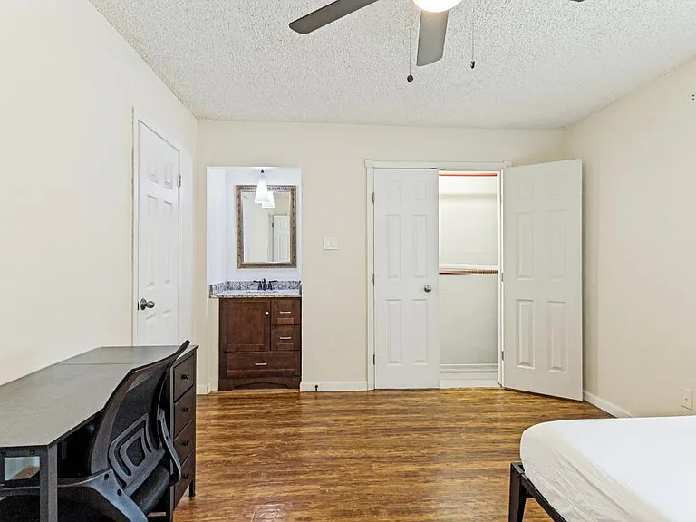 Bedroom with wood-look flooring, ceiling fan, desk area, and a vanity sink adjacent to a walk-in closet.