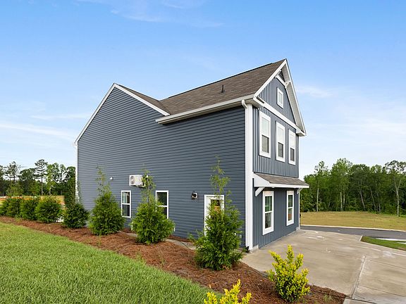 A large gray house with a garage and a driveway is sitting on top of a lush green field.
