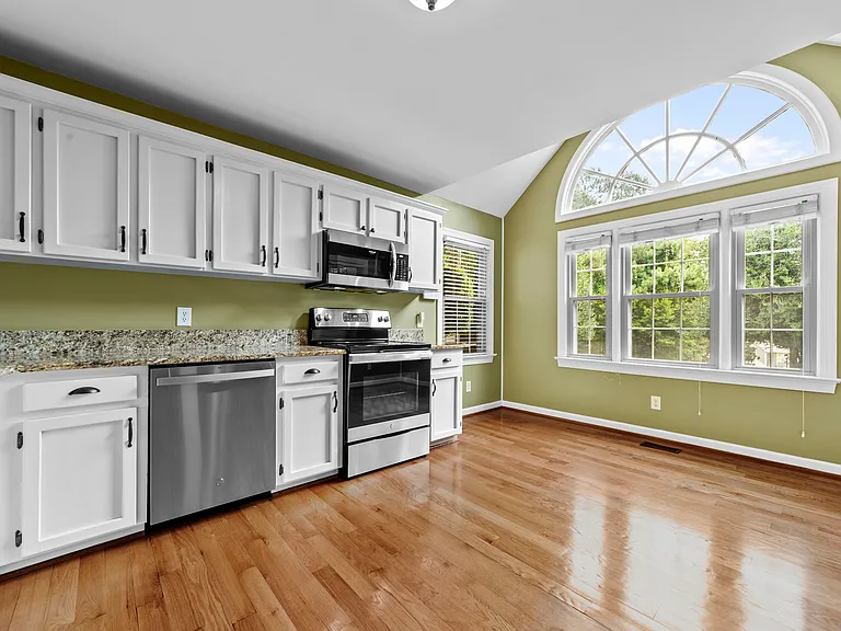 Bright kitchen with white cabinetry, granite counters, stainless steel appliances, and a dramatic arched window.