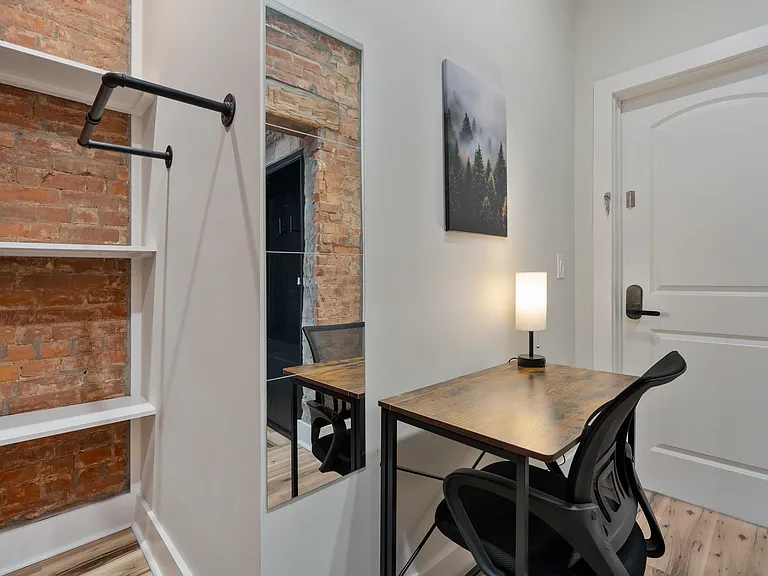 Dedicated desk nook with built-in shelving, exposed brick accent, and full-length mirror for daily convenience.